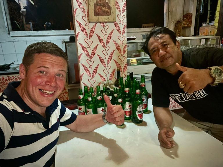 Rick Parker (Underwater Parker) with Budi at Warung Budi Ayu in Candidasa, Bali, both giving thumbs up with beers on the table