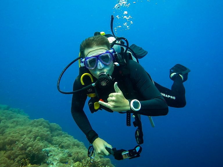 Rick Parker (Underwater Parker) facing the camera underwater, making the Wicked Sign while diving.